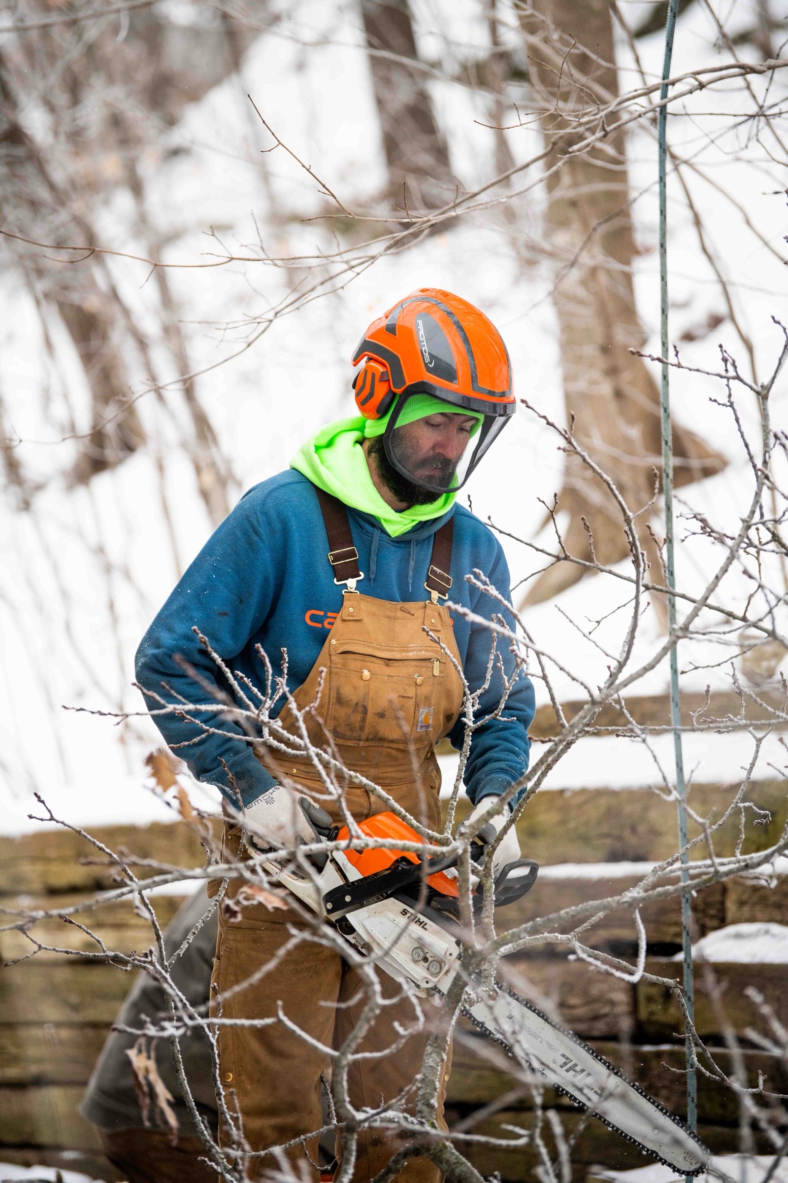 Crew member in a beanie cutting branches with a chainsaw amid frosted brush