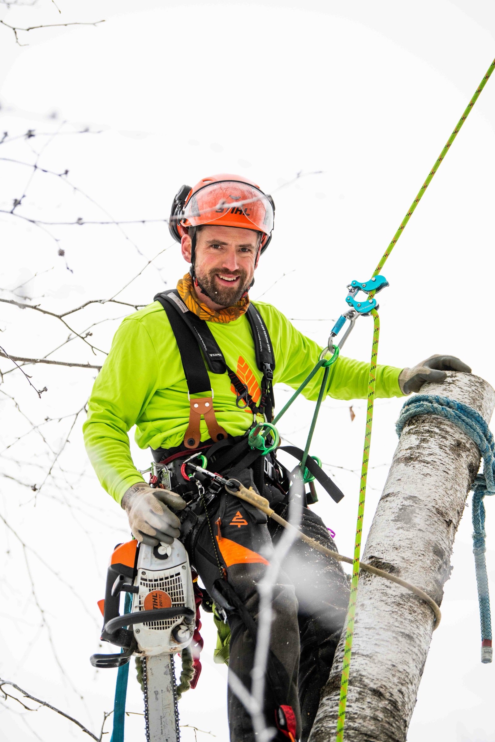 Climber smiling on a rope beside a debarked white tree trunk in the snow