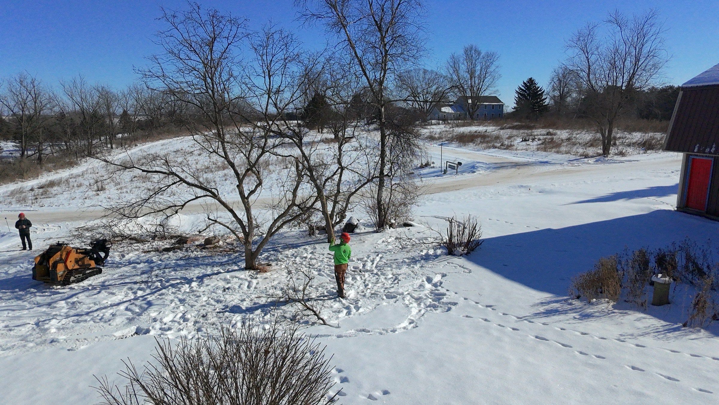 Aerial view of a crew working a leaning tree in a snowy rural yard