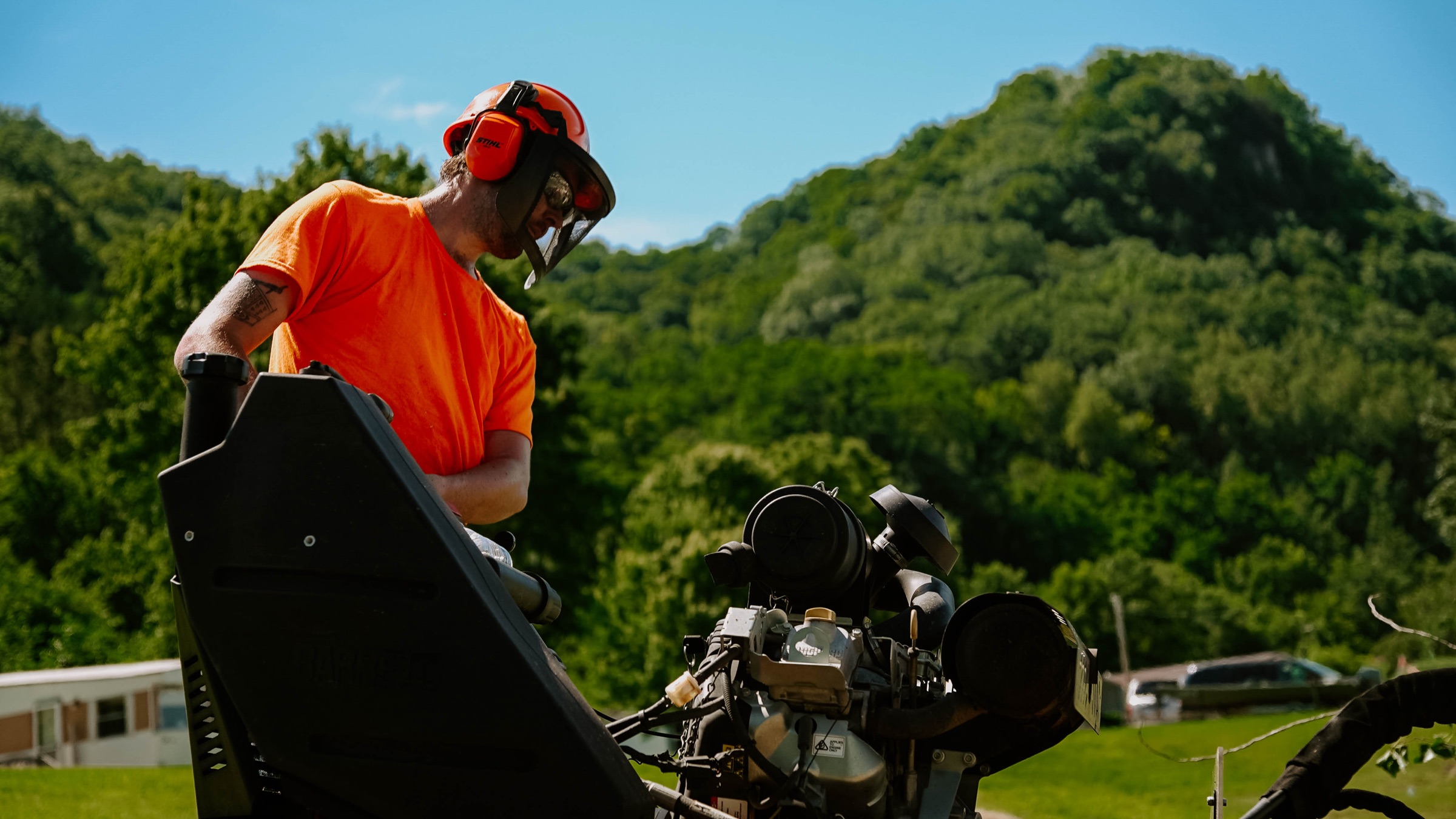 Operator running a tracked machine in a sunlit summer valley framed by green hills