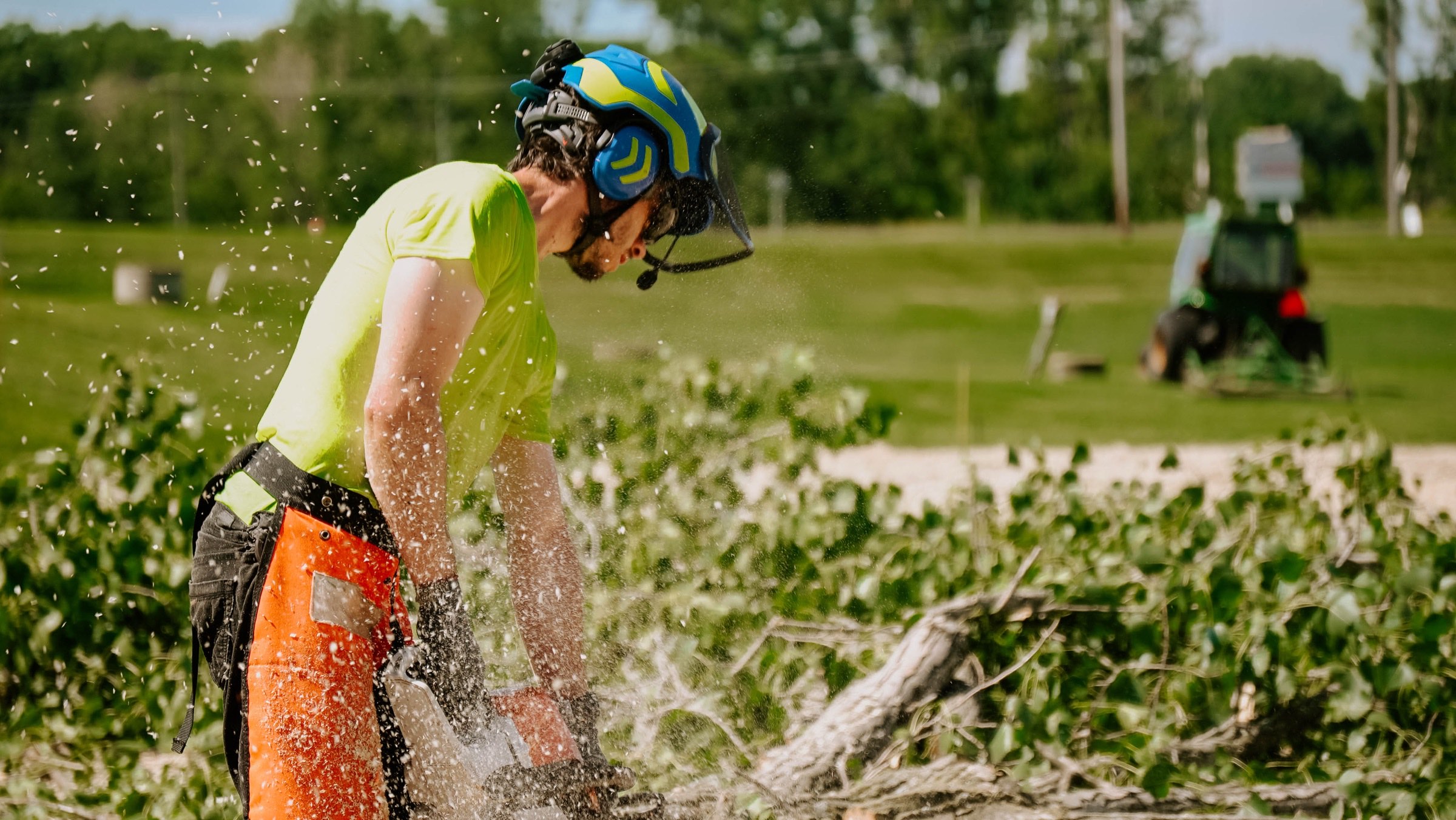 Action shot of a crew member cutting brush with wood debris flying in summer light