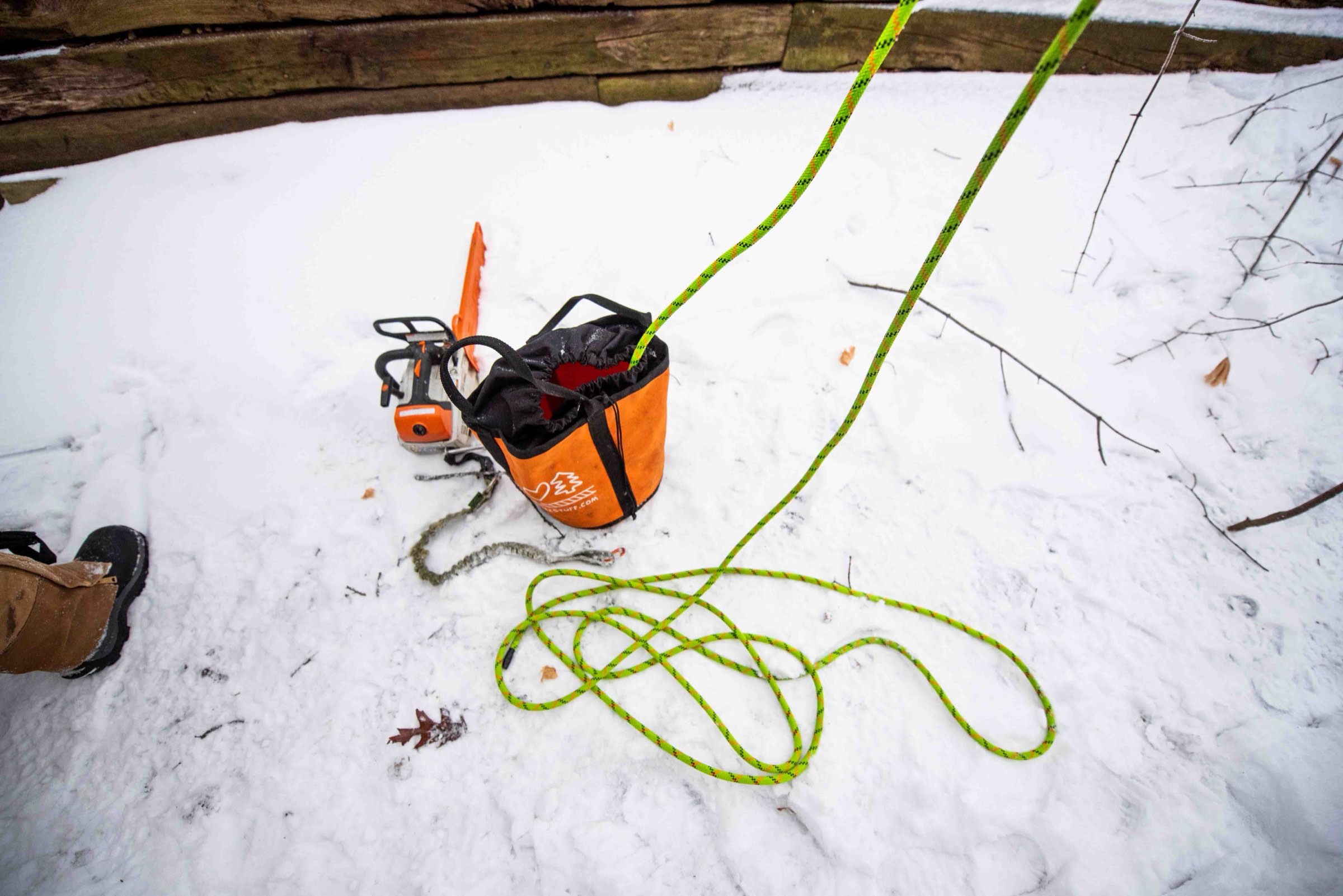Detail of an orange climbing rope bag and gear staged on snow at a winter job site